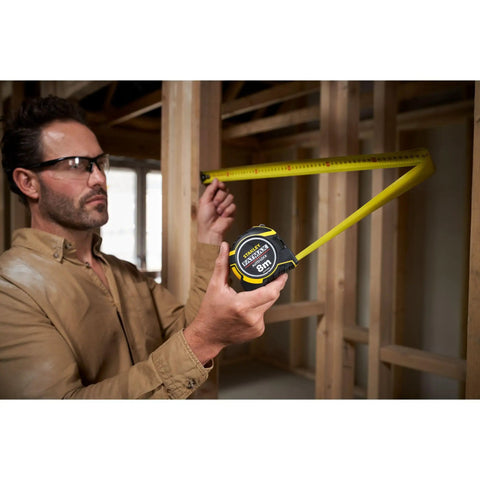 Person using Fatmax Autolock Tape Measure 8m Metric Only Yellow Black, Reverse Lock for one-handed control in construction setting