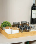 Bamboo Drawer Organizer Set Of 9 For Kitchen And Office holding mugs, jars, and containers, on a counter with wine bottles in the background.