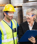 Man wearing Heavy Duty Safety Glasses Bulk Pack With Clear Lenses And Durable Blue Frames discussing with a woman in office attire.