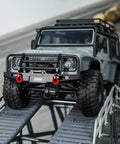 Aluminum RC Bumper Set For 1/18 TRX4M Defender on rocky slope, shows CNC Front 37G Bumper, LED lights, removable tow hitch in action.