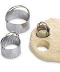 Three-piece stainless steel round cookie cutter set with handles, shown with rolled dough.