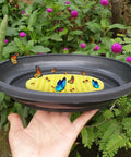 Hand holding a Four Pack Floating Bee Watering Station 7.87 Inch Island Float Tray For Pollinators with bees and butterflies.