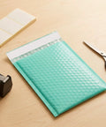 Teal 5x6 Inch Poly Bubble Mailers With Self Seal Adhesive Waterproof Padded Shipping Bags For Small Biz Packing Durable Bubble Envelopes For Secure Item Protection 100 Count on a wooden desk with scissors and tape dispenser