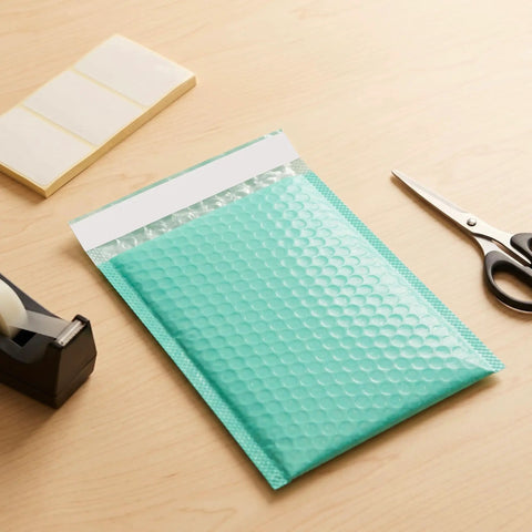 Teal 5x6 Inch Poly Bubble Mailers With Self Seal Adhesive Waterproof Padded Shipping Bags For Small Biz Packing Durable Bubble Envelopes For Secure Item Protection 100 Count on a wooden desk with scissors and tape dispenser
