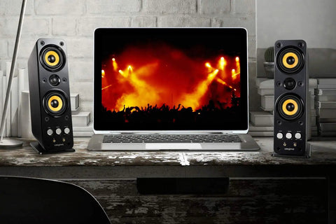 GigaWorks T40 Series II 2.0 Desktop Speaker System with BasXPort Tech beside a laptop showing a concert scene on a wooden desk