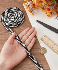 Black and white cord held by hand with ruler, coin, scissors, and orange flowers on wooden table