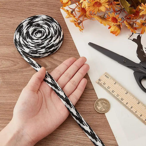Black and white cord held by hand with ruler, coin, scissors, and orange flowers on wooden table