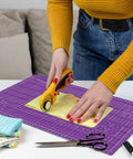 Front view of Headley Tools purple 18x12 inch self-healing cutting mat; rotary cutter cutting fabric on it