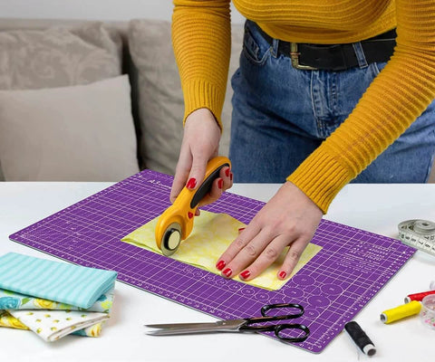 Front view of Headley Tools purple 18x12 inch self-healing cutting mat; rotary cutter cutting fabric on it
