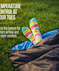Feet in colorful socks sticking out of Three Season XXL Backpacking Sleeping Bag For Adults And Kids, Lightweight And Water Resistant.