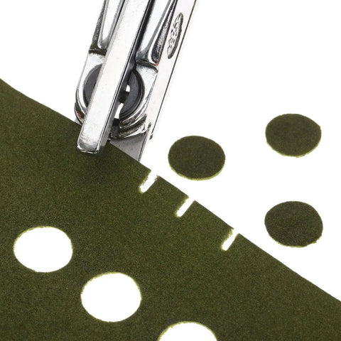 Close-up of Hand Held Slot And Thirteen Millimeter Round Hole Punch Tool 2-In-1 Diy Puncher on green paper