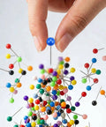 Hand holding a blue Straight Up Go To Multi Color Map Push Pin above colorful pins for travel boards, showcasing 100 markers.