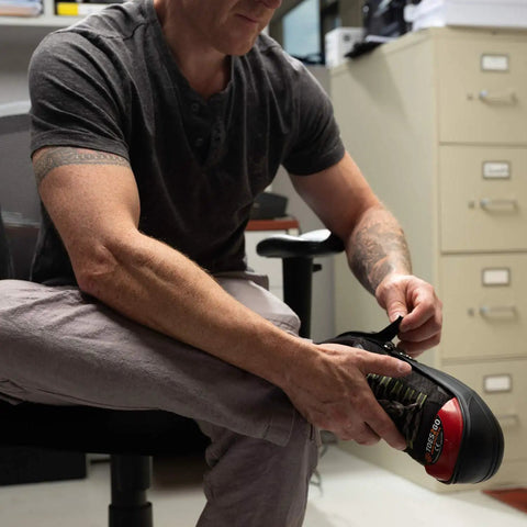 Man adjusting Red Steel Toe Cap Overshoe Med Over Shoe With Adjustable Straps Waterproof PVC Non Slip Protects Feet From Impact And Crushing Fits M8-13 And W10-13 Ideal For Work Visitors And Casual Use in office setting.