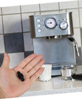 Hand holding Steam Wand Heat Shield Rubber Sleeve For Espresso Machines in front of a coffee maker showcasing the anti scald guard.