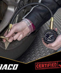 JACO EliteProPlus tire pressure gauge with dually air chuck used on a car tire; black dial gauge with brass fittings.