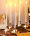 24 Pack Flameless Taper Candles With Remote And Timer, Flickering 3D Flame LED Tapers in silver bases on a wooden table