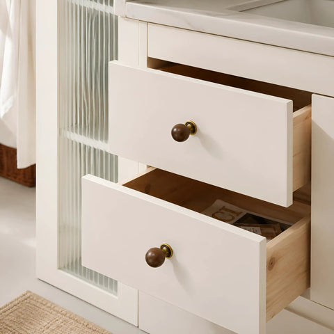 The Real Deal Natural Walnut And Antique Brass Cabinet Knobs Six Pack on white kitchen drawers, featuring round ball handles for easy use.