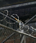 Chain link fence with barbed wire under industrial structure, featuring pipe track gate roller detail in heavy-duty setting.