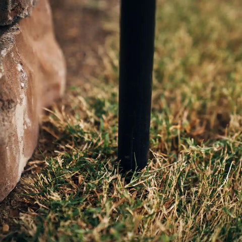 Close-up of steel stake installed in grass for Adjustable Swivel Grill Grate For Open Fire Cooking With Spike Pole Steel Mesh Wire Grate