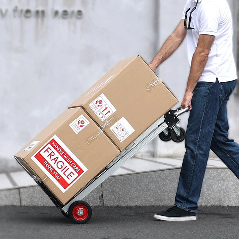Aluminum folding hand truck with red wheels carrying two cardboard boxes labeled FRAGILE.