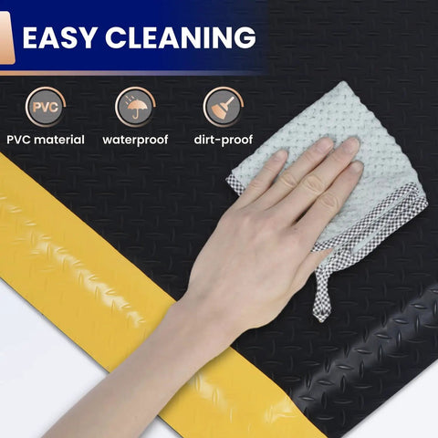 Anti Fatigue Standing Mat For Workshops 3 By 5 Feet Beefed Up Industrial Grade Ergonomic Floor Mat Nearly One Inch Thick With Non Slip Surface And Yellow Border For Leg And Back Pain Relief On Long Shifts, close-up of hand cleaning the non-slip surface.