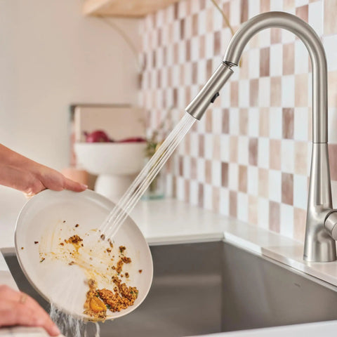 Top Shelf Pulldown Kitchen Faucet In Slick Spot Resist Stainless Steel washing food residue off a plate with 360 swivel spray wand.