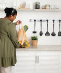 Woman in kitchen placing groceries on counter with hanging black kitchen utensils in background