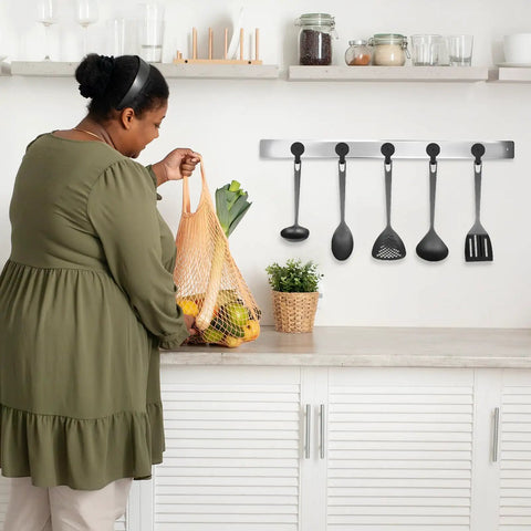 Woman in kitchen placing groceries on counter with hanging black kitchen utensils in background