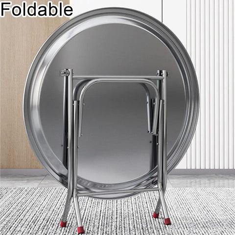 Ultra Strong Stainless Steel Folding Work Table With Thick Silicone Floor Pads And Premium Brushed Finish X Beam Reinforcement For No Sweat Garage Or Backyard Projects standing against a wall.