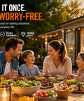 Family enjoying dinner outdoors at a wooden table, with various dishes and drinks, in a cozy evening setting.