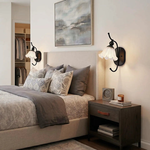 PUMING Black Wall Sconces Set of Two beside a bed, featuring flower glass shades and black metal frame in a cozy bedroom.
