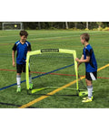 Two children setting up a Portable Backyard Soccer Goal Small Size Pop Up With Quick Setup Durable Fiberglass Frame All Weather Practice Net on a field.