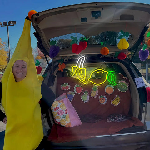 Person in banana costume next to car display with Bright Dope Banana Shaped LED Neon Sign Light For Bedroom Decor, 11 by 19.7 Inches