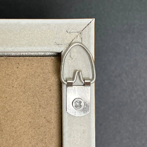 D ring hanger with slotted screw on frame corner, part of 100 Pack D Ring Picture Hangers With Screws For Hanging Frames Mirrors Clocks Paintings Ten Pound Load Support One And A Quarter Inch Long Five Eighths Inch Wide Bulk Pack Includes 100 Six By One Half Inch Slotted Phillips Combo Screws