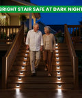 Elderly couple descending stairs with Solar Powered Fence Lights 12 Pack Outdoor Deck Lights Waterproof Stainless Steel Security Wall Lamps illuminating steps at night.