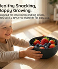 Child holding black bowl filled with strawberries and blueberries from Built Tough 36 Piece Wheat Straw Dinnerware Set For 6 No Fuss Unbreakable Bowls Plates And Cups Dishware Safe For Dishwasher And Microwave Ideal For Outdoor Camping Black.