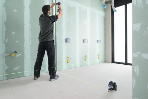Pro Level 12V Green Beam Cross Line Laser With 100 Foot Reach in use for precision alignment on drywall installation.