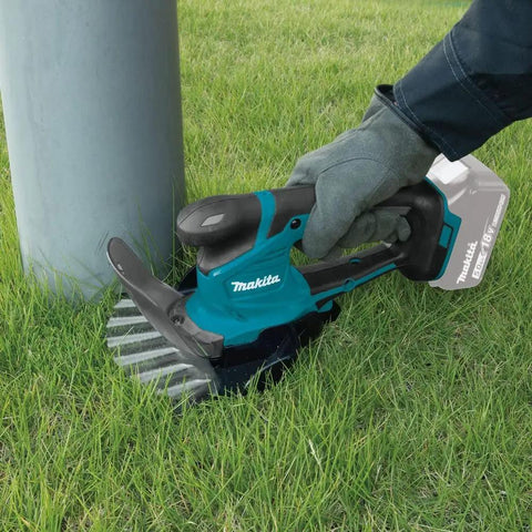 18V LXT Cordless Grass Shear with Hedge Trimmer Blade trimming grass around a pole, tool only, renewed, gloved hand in use.