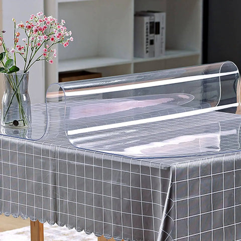 Clear 24 By 60 Inch Table Protector 1.5mm Thick PVC Desk Mat shown partially rolled on a table with a vase and shelf in the background.