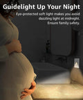 Close-up of a pregnant woman with her hand on her belly, illuminated by a soft LED night light from a wall outlet.