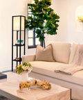 Maxwell Shelf Floor Lamp With USB Ports, Wireless Charging Pad, And Built In Outlet in a modern living room with white sofa
