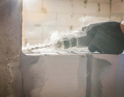 Side view of SDS‑Plus carbide-tipped drill bit drilling into concrete block with a hammer drill