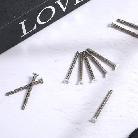 Forty Pack Super Long Outlet Screws Two Inch Flat Head White Painted Stainless Steel Machine Threads For Electric Box Hardware Quick Fix, scattered screws on a white surface.