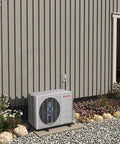 No Sweat Cooling 12000 Btu Mini Split Air Conditioner And Inverter Heat Pump installed outside on a gravel landscape with flowers.