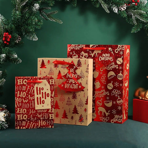 Festive gift bags with holiday designs next to pine branches, no visible 12 Piece Set Of Large Kraft White Gift Bags With Red Paper Accents.