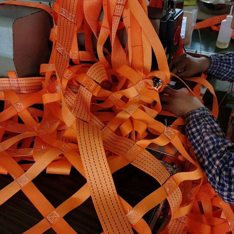 Orange flat nylon lifting slings tangled on a workbench for hoisting and rigging.