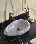 Sleek Marble Vessel Sink For Modern Bathrooms Featuring An Oval Countertop Basin Design on black surface with faucet and decor.