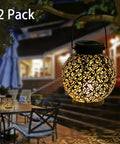 Outdoor Solar Lanterns Hanging Lights For Patio Porch Backyard Decorative Garden Lamps Metal Waterproof LED Lanterns With Auto On Off No Fuss Easy Setup Create Charming Shadow Patterns Two Pack illuminating a garden seating area at night.