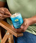 Person holding lit Citronella Mosquito Repellent Candle Pack Of 2 For Outdoor Adventures Camping With Essential Oils Soybean And Beeswax Burns 18 Hours DEET Free Naturally Scented With Rosemary And Lemongrass For Outdoor Relaxation.