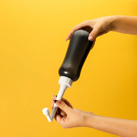 Hands holding a MicroJet MJ 450 Portable Bidet And Peri Bottle Sprayer For Travel with ergonomic squeeze and angled nozzle.